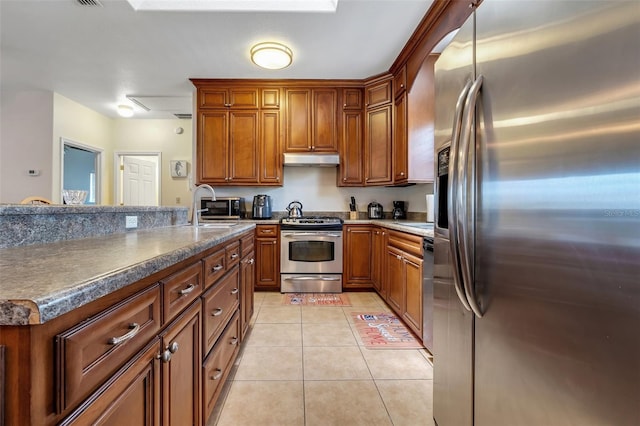 kitchen with a sink, under cabinet range hood, brown cabinets, stainless steel appliances, and light tile patterned flooring