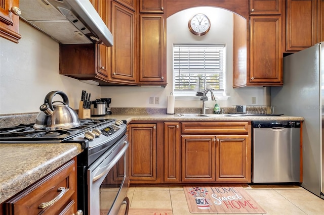 kitchen with light tile patterned floors, brown cabinetry, appliances with stainless steel finishes, under cabinet range hood, and a sink