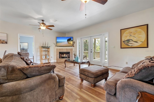 living room featuring a tiled fireplace, light wood-style floors, visible vents, and a ceiling fan