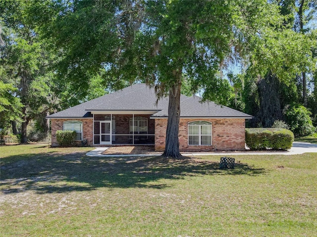 single story home with a sunroom, roof with shingles, a front yard, and brick siding