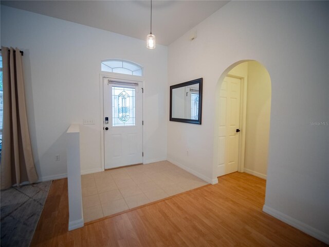 foyer featuring arched walkways, light wood finished floors, and baseboards