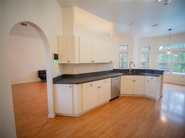 kitchen with a peninsula, dark countertops, light wood-style floors, stainless steel dishwasher, and a sink