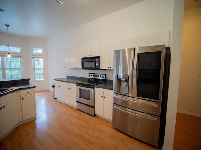 kitchen featuring stainless steel appliances, light wood finished floors, pendant lighting, and dark countertops