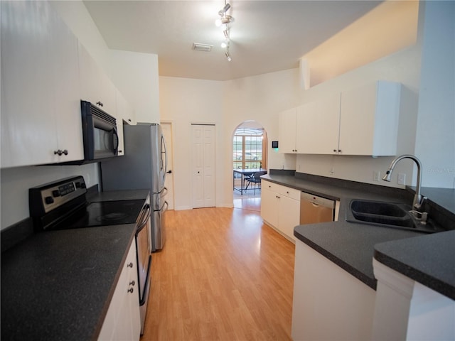 kitchen featuring arched walkways, a sink, dark countertops, light wood-style floors, and stainless steel appliances