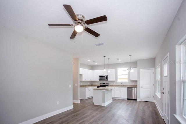 kitchen with baseboards, a sink, appliances with stainless steel finishes, dark wood-type flooring, and a kitchen island