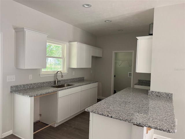 kitchen with a peninsula, a sink, dark wood-style flooring, white cabinetry, and light stone counters