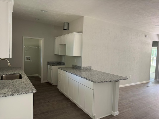 kitchen featuring a sink, baseboards, white cabinetry, light stone counters, and dark wood-type flooring