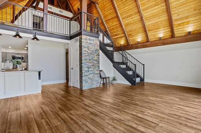 unfurnished living room with wood finished floors, high vaulted ceiling, baseboards, and stairway