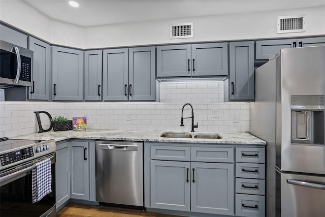 kitchen featuring visible vents, appliances with stainless steel finishes, light stone counters, a sink, and gray cabinetry