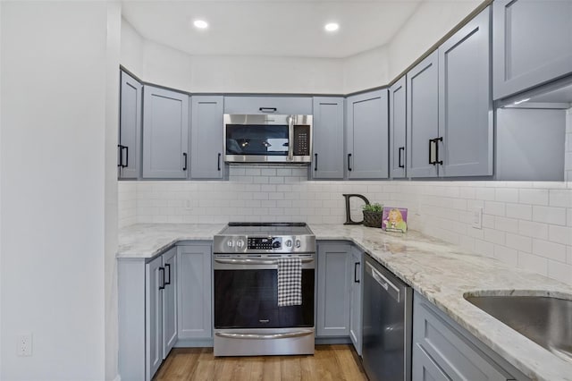 kitchen featuring gray cabinets, light wood-style flooring, backsplash, light stone countertops, and appliances with stainless steel finishes