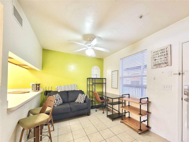 living area with light tile patterned flooring, visible vents, a ceiling fan, and baseboards
