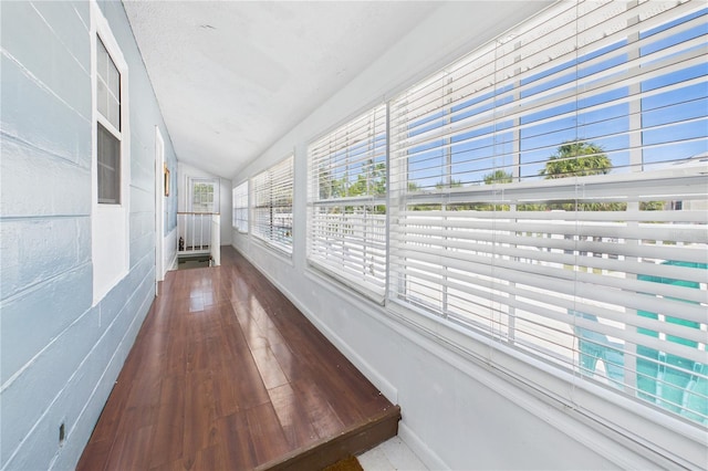 unfurnished sunroom featuring baseboards, vaulted ceiling, and wood finished floors