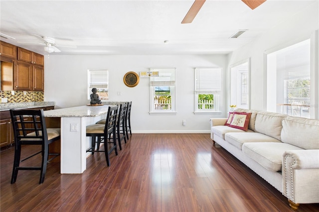 living room with dark wood-type flooring, visible vents, baseboards, and a ceiling fan