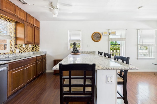 kitchen featuring black electric cooktop, dishwasher, dark wood-style flooring, a kitchen breakfast bar, and backsplash