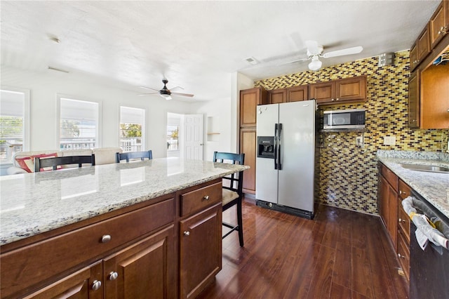 kitchen featuring fridge with ice dispenser, a kitchen bar, ceiling fan, and stainless steel microwave