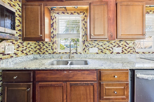 kitchen with stainless steel microwave, light stone countertops, a sink, and backsplash