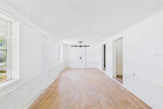 unfurnished room featuring a healthy amount of sunlight, light wood-type flooring, baseboards, and a textured ceiling