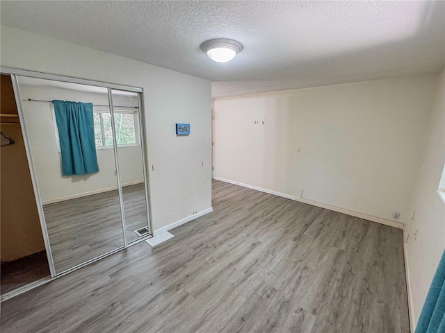 3935 SW 26th Ter Unit 3935A, Gainesville, FL 32608 - unfurnished bedroom featuring a textured ceiling, baseboards, a closet, and wood finished floors
