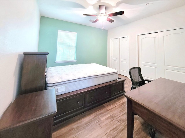 bedroom featuring two closets, light wood-type flooring, an office area, and ceiling fan