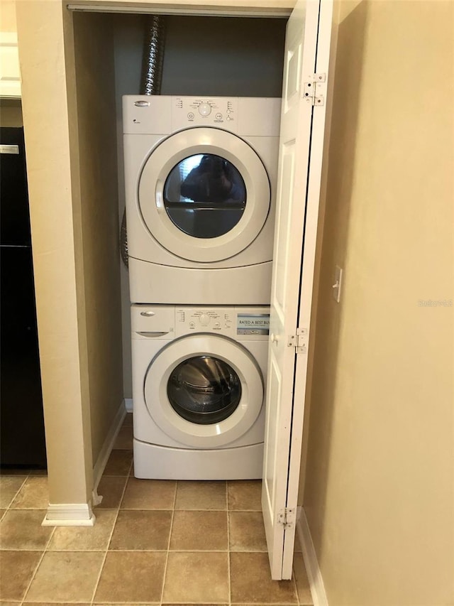 washroom with laundry area, light tile patterned flooring, stacked washer / drying machine, and baseboards