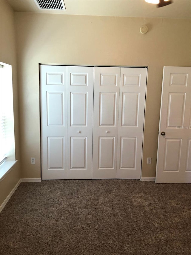 unfurnished bedroom featuring dark colored carpet, baseboards, a closet, and visible vents