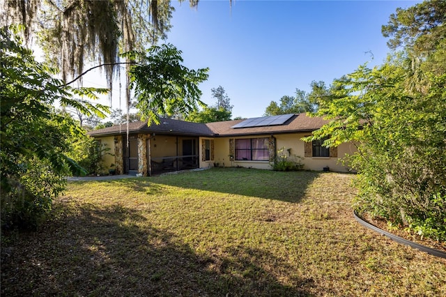 rear view of house with stucco siding, a lawn, a sunroom, and solar panels