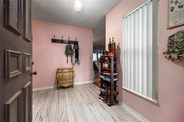 mudroom featuring light wood finished floors, baseboards, and a textured ceiling
