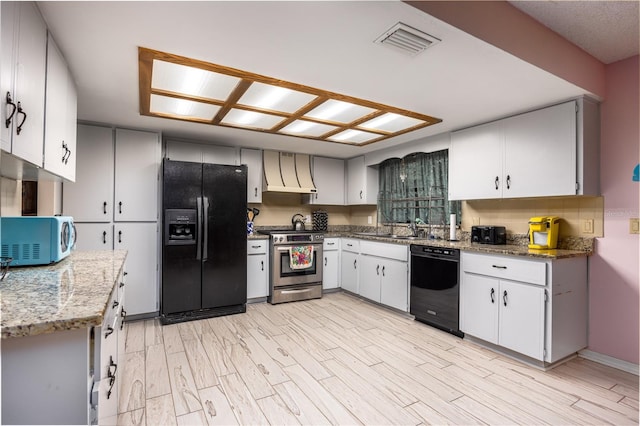 kitchen with light wood finished floors, visible vents, premium range hood, light stone countertops, and black appliances