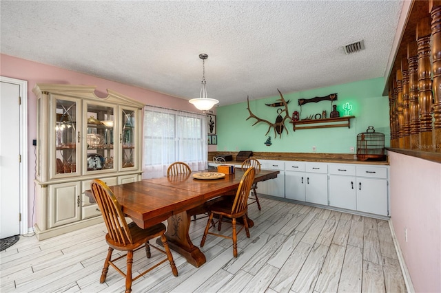 dining room with light wood-style floors, a textured ceiling, and visible vents