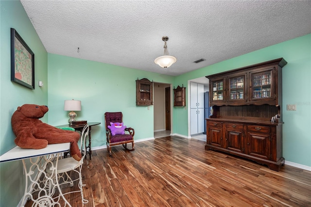 living area with baseboards, wood finished floors, visible vents, and a textured ceiling