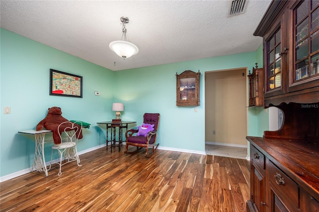 living area with a textured ceiling, wood finished floors, visible vents, and baseboards