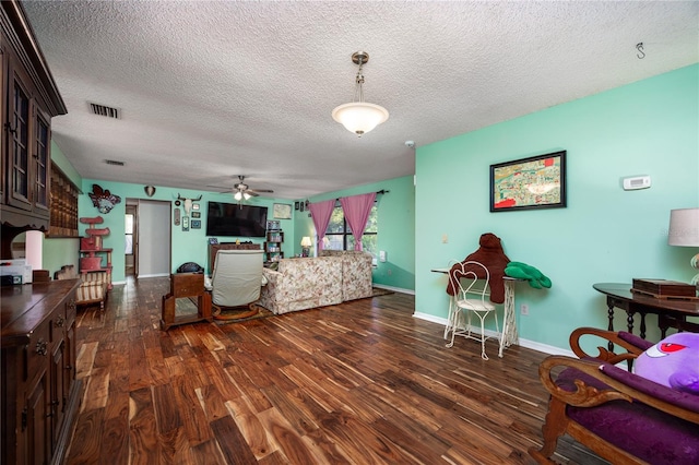 living area featuring wood finished floors, a textured ceiling, ceiling fan, baseboards, and visible vents