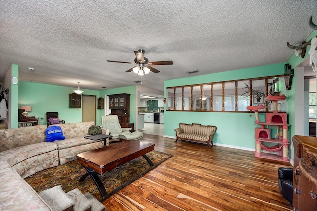 living area featuring baseboards, a ceiling fan, wood finished floors, and a textured ceiling