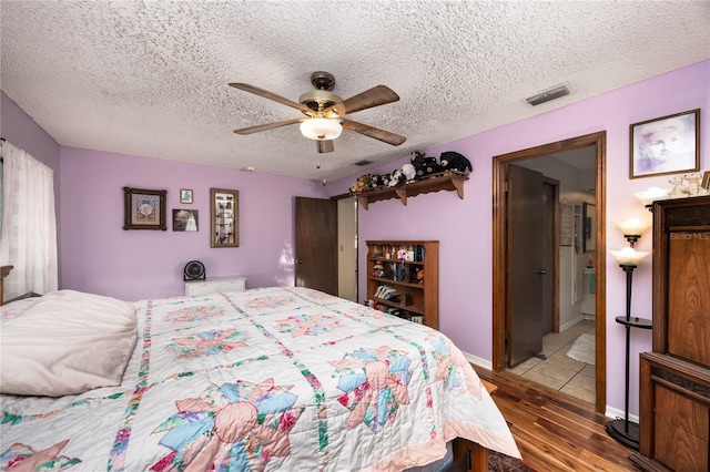 bedroom with a textured ceiling, wood finished floors, visible vents, and a ceiling fan