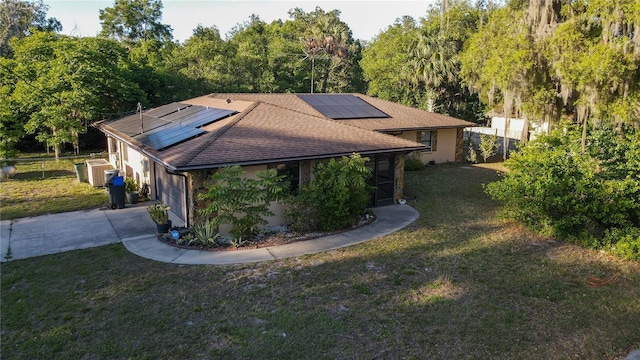 exterior space with concrete driveway, fence, a lawn, a shingled roof, and roof mounted solar panels