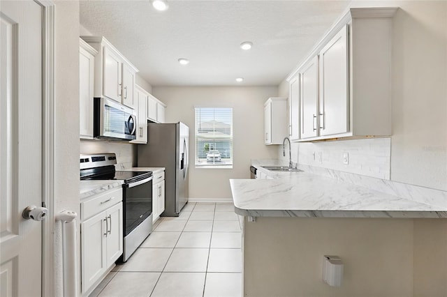 kitchen featuring appliances with stainless steel finishes, a peninsula, light tile patterned floors, decorative backsplash, and a sink