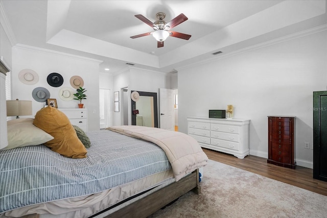 bedroom featuring crown molding, wood finished floors, a tray ceiling, and visible vents