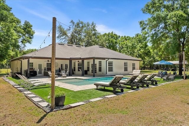rear view of property featuring an outdoor pool, a ceiling fan, french doors, a yard, and a patio