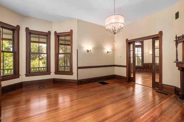 spare room with plenty of natural light, wood-type flooring, a notable chandelier, and baseboards