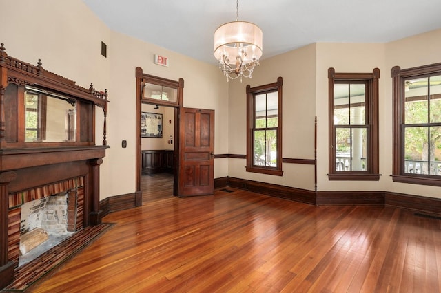 unfurnished living room with a chandelier, a fireplace, wood-type flooring, and baseboards