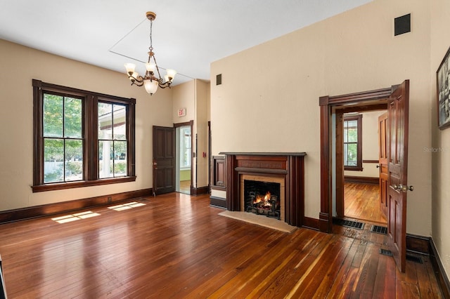 unfurnished living room featuring a warm lit fireplace, wood-type flooring, baseboards, and an inviting chandelier