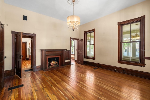 unfurnished living room with a lit fireplace, baseboards, a chandelier, visible vents, and wood-type flooring