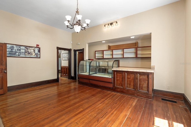 unfurnished dining area with hardwood / wood-style floors, an inviting chandelier, baseboards, and visible vents