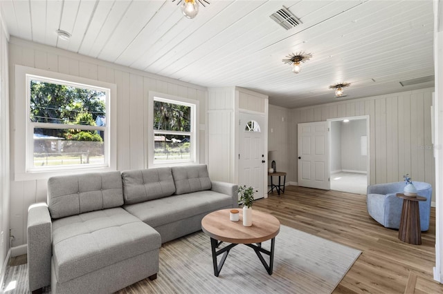living room with wood walls, visible vents, wooden ceiling, light wood-type flooring, and baseboards