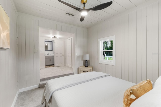 carpeted bedroom with visible vents, wood walls, baseboards, and ensuite bathroom