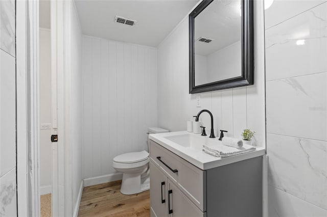 half bathroom with wood finished floors, visible vents, vanity, and toilet