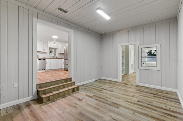 spare room featuring a sink, light wood finished floors, baseboards, wood walls, and visible vents