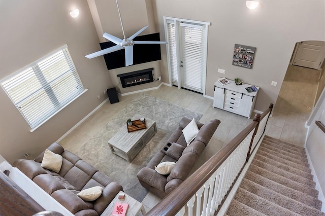living room featuring a ceiling fan, baseboards, a glass covered fireplace, and plenty of natural light