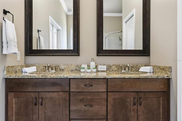 bathroom with crown molding, a shower with shower door, double vanity, and a sink