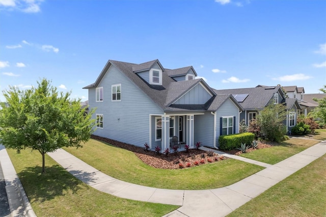 view of front of house featuring roof mounted solar panels, a shingled roof, board and batten siding, and a front yard